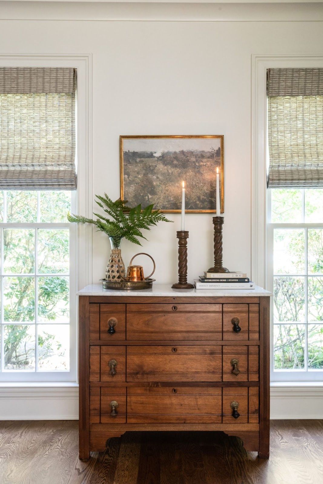 Wood pine chest with marble top. Candles, and decor sit on top and vintage artwork hangs above. 
